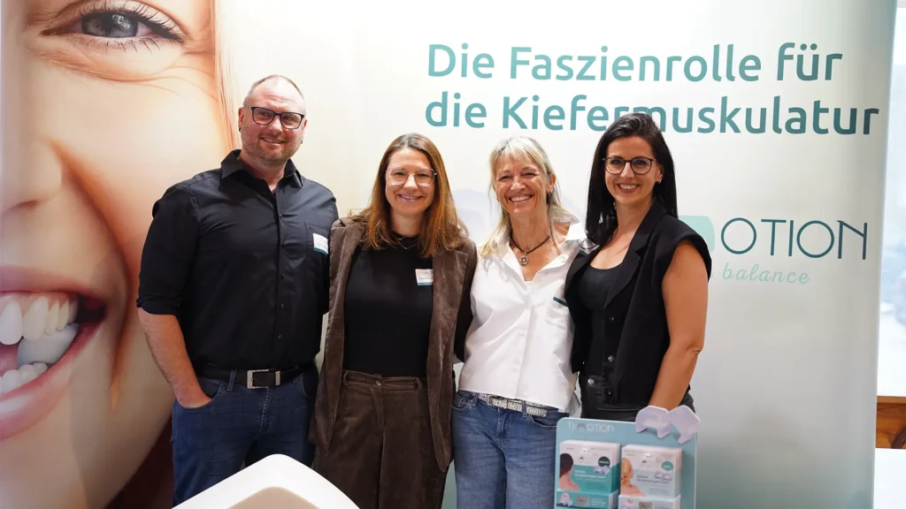 Vier Personen stehen vor dem TJ-Motion-Messestand und präsentieren gemeinsam die Faszienrolle für die Kiefermuskulatur.