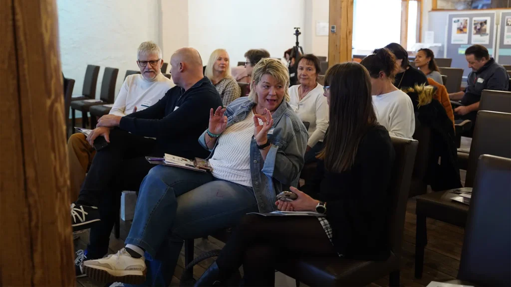 Teilnehmende sitzen in einem Veranstaltungsraum und unterhalten sich vor Beginn eines Vortrags über das Thema Kiefergesundheit.