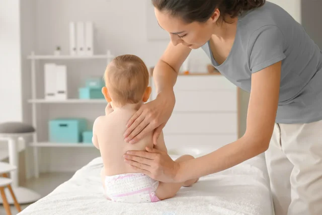 Physiotherapeutin behandelt ein Baby mit Entwicklungsverzögerung in einer hellen Praxis während einer Kinder- und Säuglingstherapie nach Bobath.
