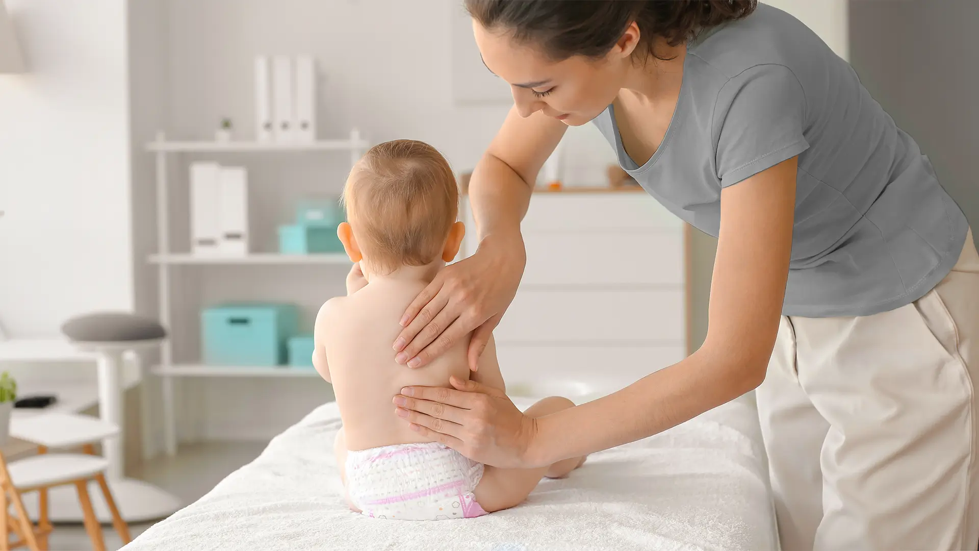 Physiotherapeutin behandelt ein Baby mit Entwicklungsverzögerung in einer hellen Praxis während einer Kinder- und Säuglingstherapie nach Bobath.